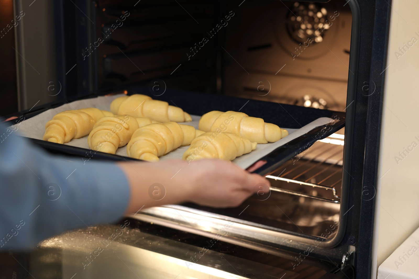 Woman putting baking sheet with raw croissants into oven, closeup Photo of Woman putting baking sheet with raw croissants into oven, closeup