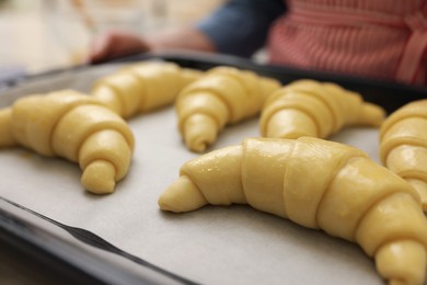 Woman holding baking sheet with raw croissants, selective focus