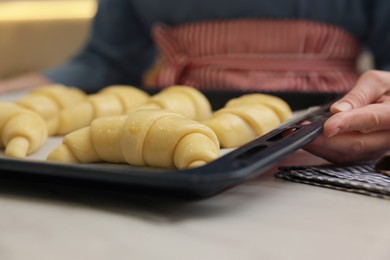 Photo of Woman taking baking sheet with raw croissants out of white table, selective focus