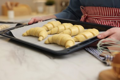 Photo of Woman taking baking sheet with raw croissants out of white marble table, closeup