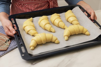 Photo of Woman taking baking sheet with raw croissants out of white marble table, closeup