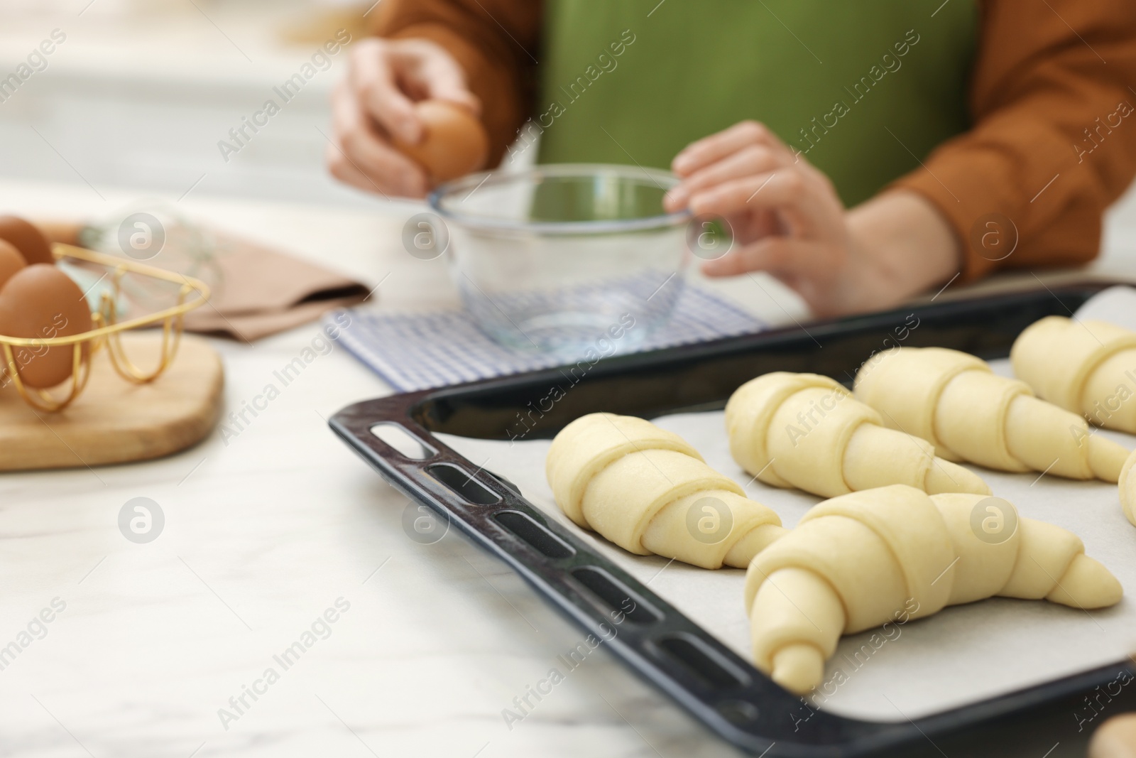 Woman breaking egg into bowl near raw croissants at white marble table indoors, selective focus Photo of Woman breaking egg into bowl near raw croissants at white marble table indoors, selective focus