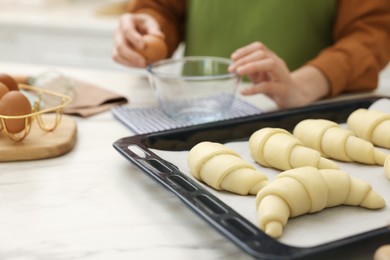 Photo of Woman breaking egg into bowl near raw croissants at white marble table indoors, selective focus