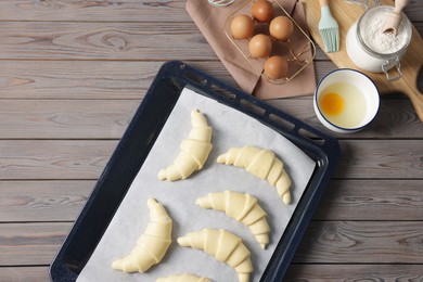 Photo of Raw croissants, ingredients and kitchenware on wooden table, flat lay