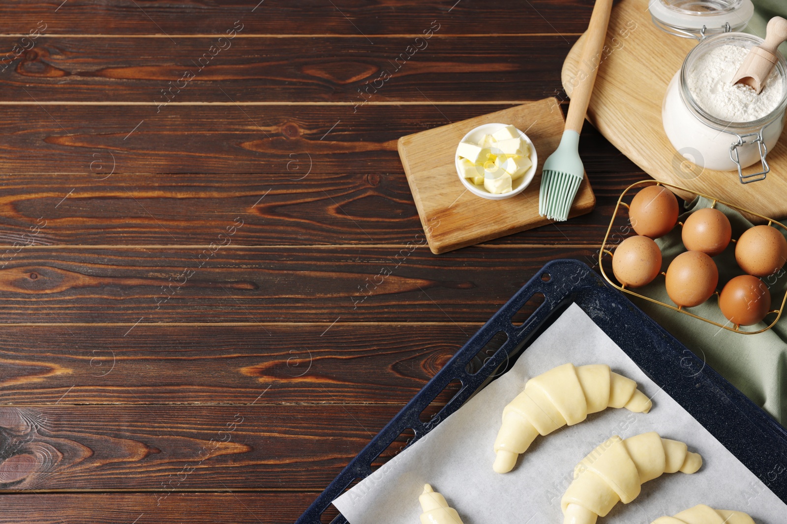 Photo of Raw croissants, ingredients and kitchenware on wooden table, flat lay. Space for text