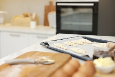 Photo of Raw croissants and ingredients on white table in kitchen, selective focus