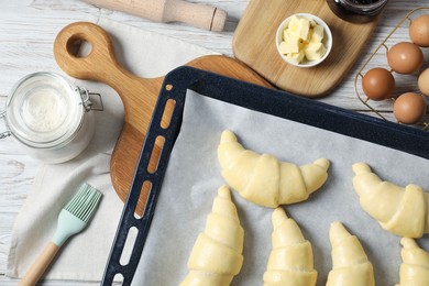 Raw croissants, ingredients and kitchenware on wooden table, flat lay