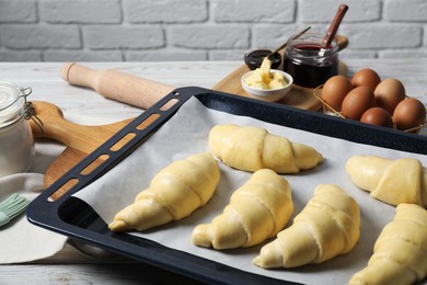 Raw croissants, ingredients and kitchenware on wooden table against brick wall, closeup