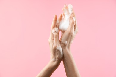 Photo of Woman washing hands with foaming soap on pink background, closeup. Hygiene