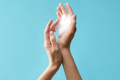 Photo of Woman washing hands with foaming soap on light blue background, closeup. Hygiene