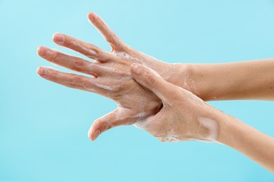 Photo of Woman washing hands with foaming soap on light blue background, closeup. Hygiene