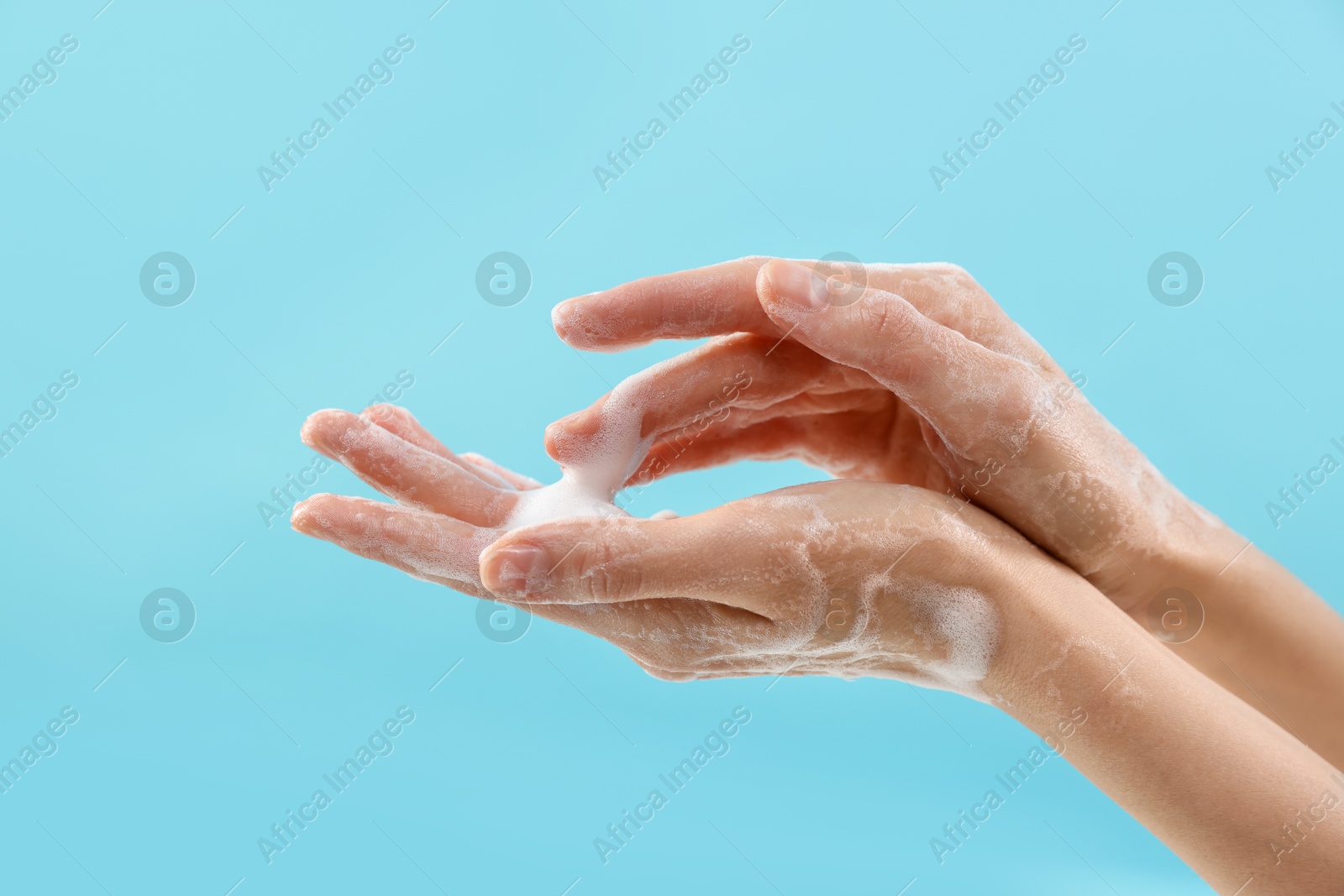 Photo of Woman washing hands with foaming soap on light blue background, closeup. Hygiene