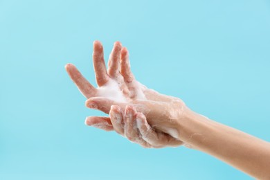 Photo of Woman washing hands with foaming soap on light blue background, closeup. Hygiene