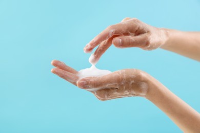 Photo of Woman washing hands with foaming soap on light blue background, closeup. Hygiene