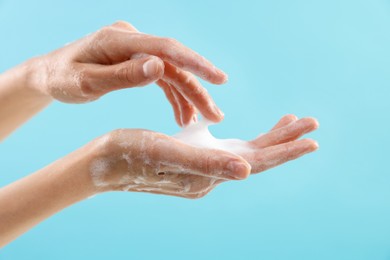 Photo of Woman washing hands with foaming soap on light blue background, closeup. Hygiene