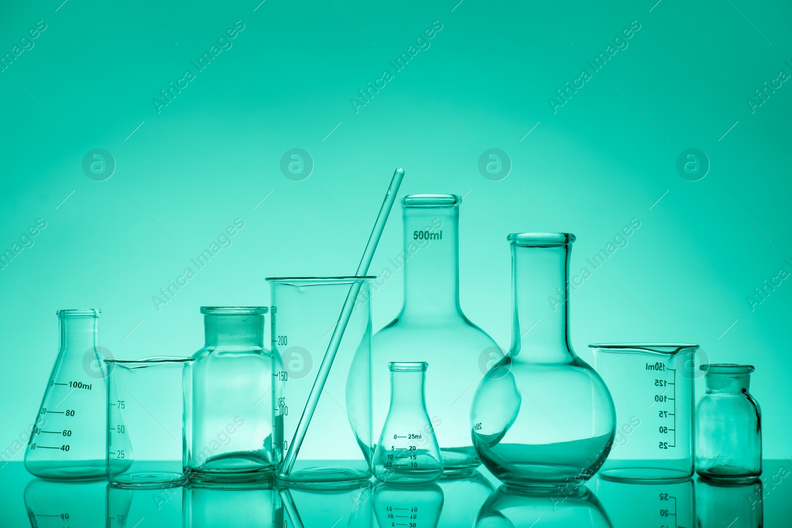 Photo of Laboratory glassware on mirror surface against green background