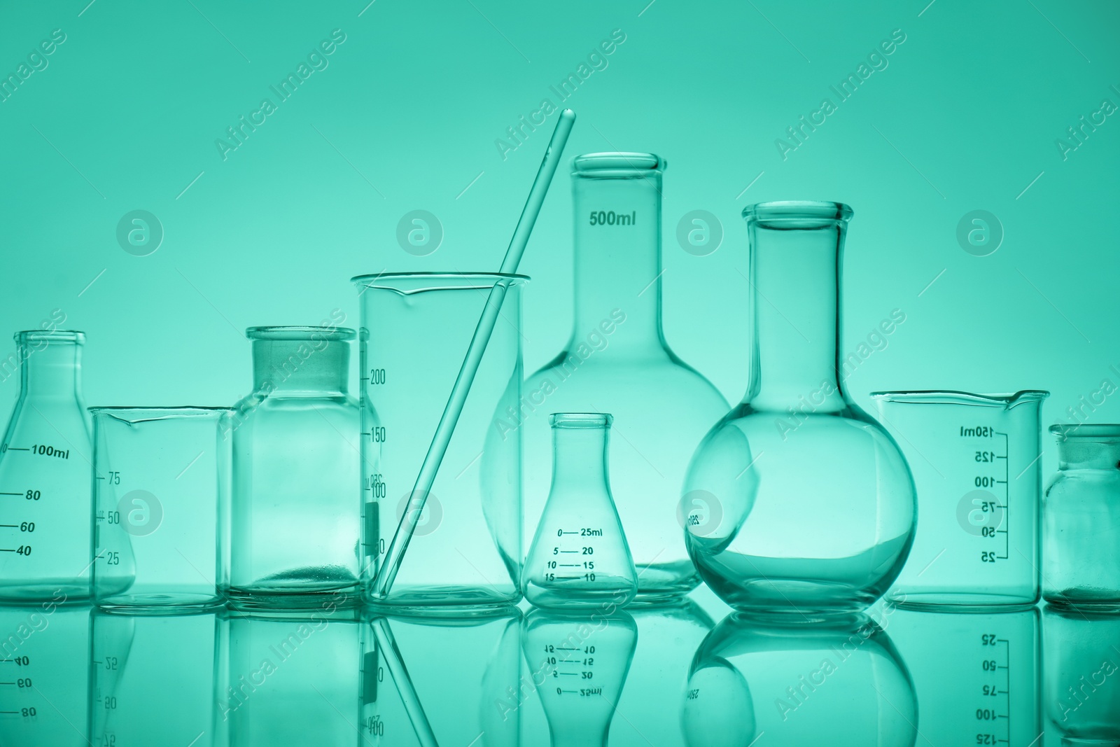 Photo of Laboratory glassware on mirror surface against green background