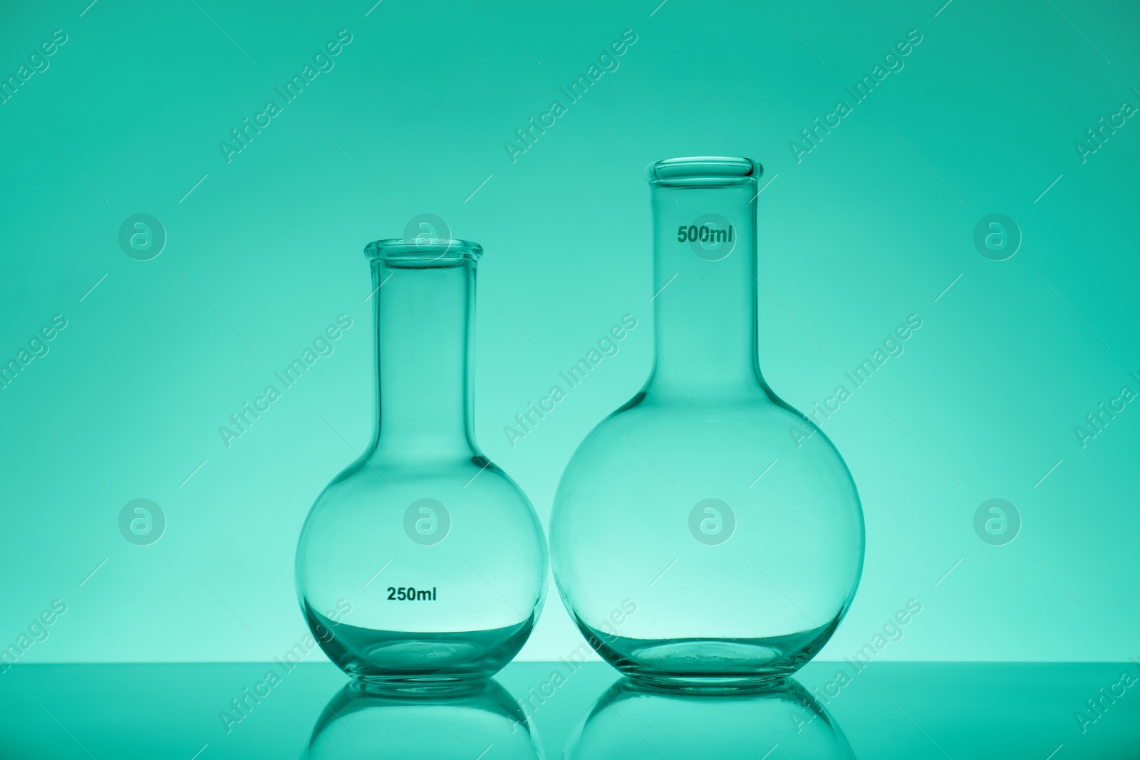 Photo of Empty flasks on mirror surface against green background. Laboratory equipment