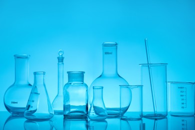 Photo of Laboratory glassware on mirror surface against light blue background