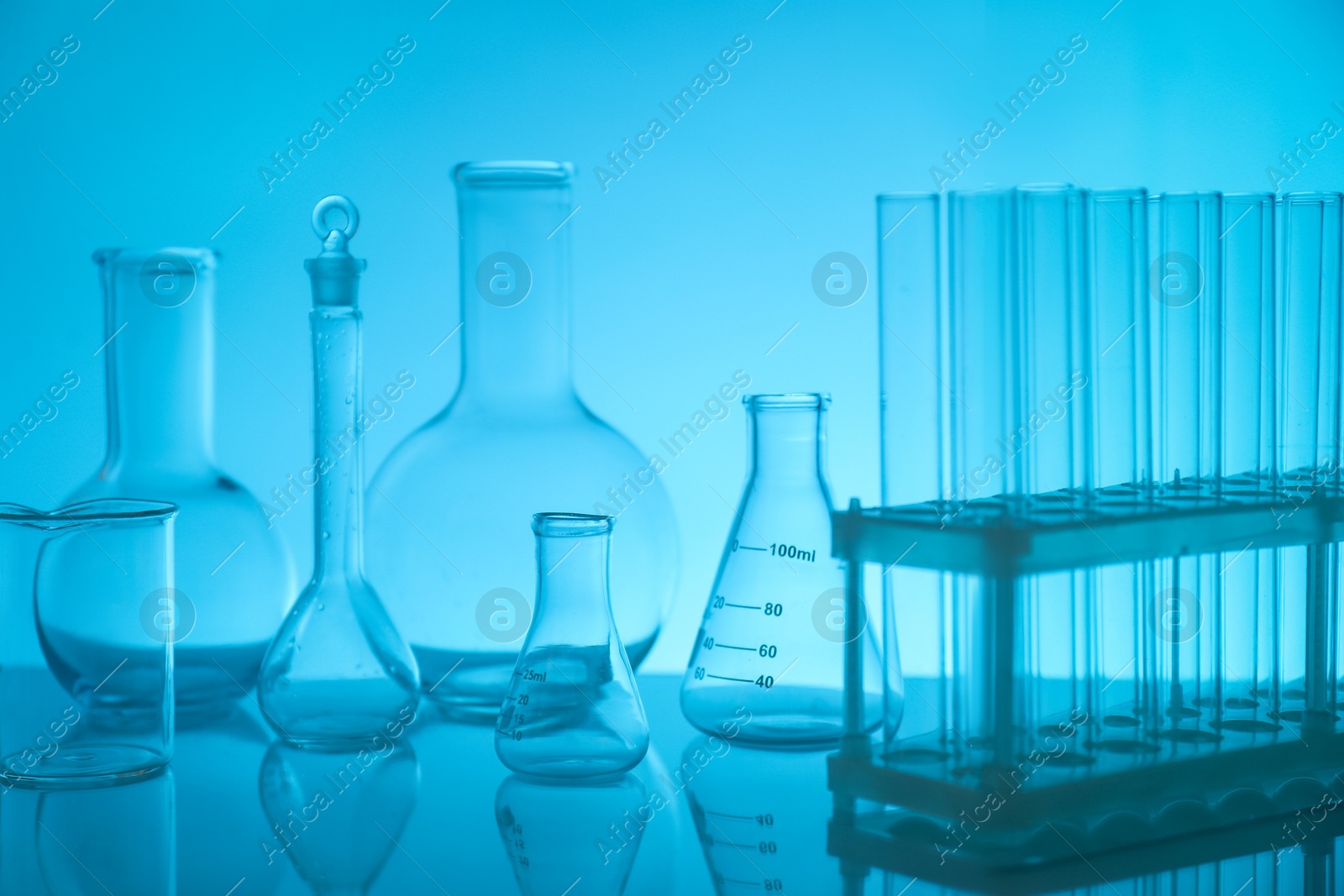 Photo of Laboratory glassware on mirror surface against light blue background