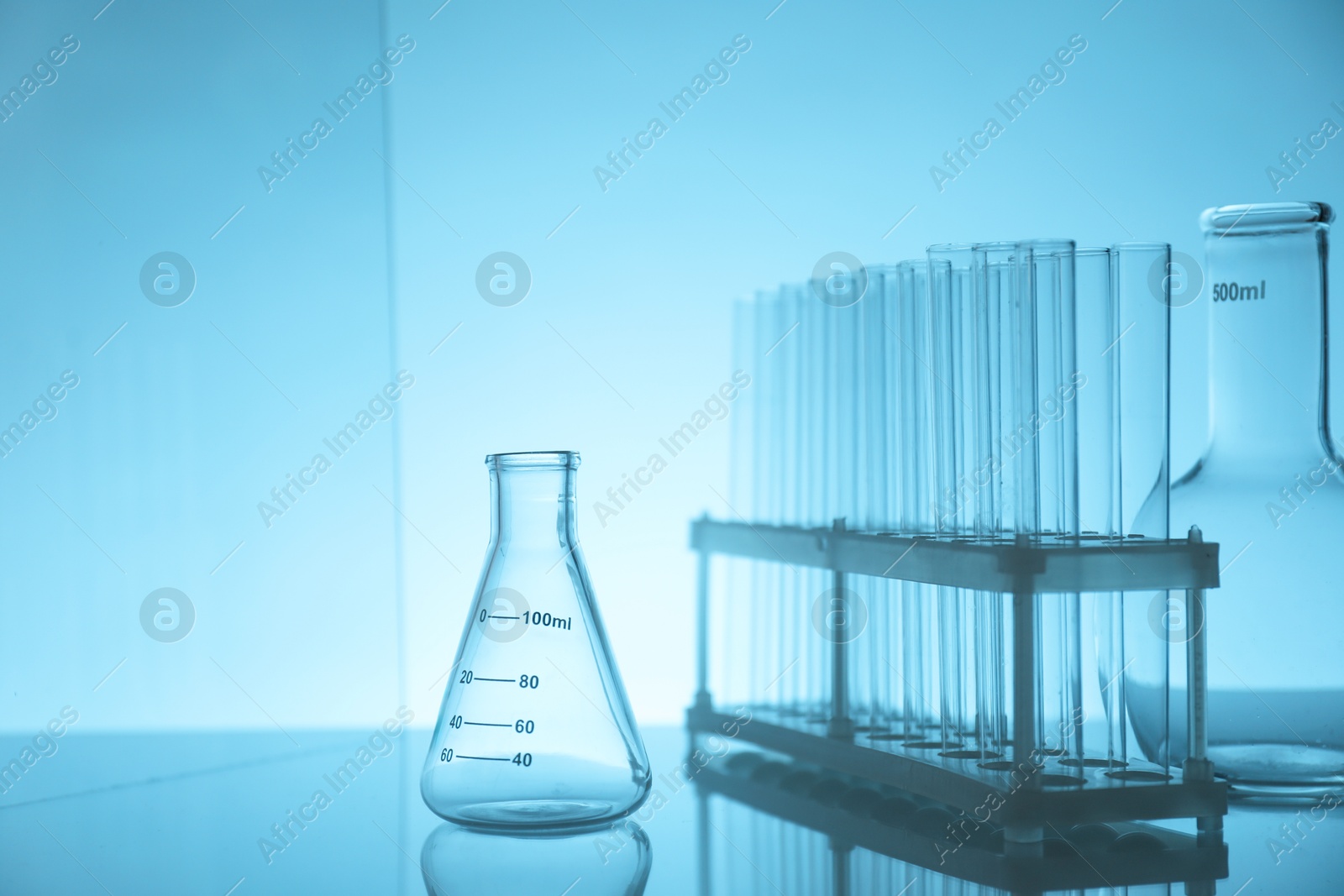 Photo of Laboratory glassware on mirror surface against light blue background