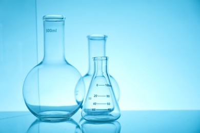 Empty flasks on mirror surface against light blue background, space for text. Laboratory equipment