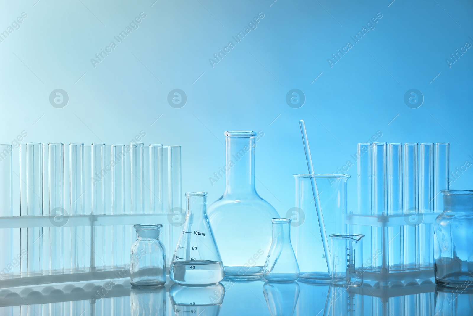 Photo of Laboratory glassware on mirror surface against light blue background