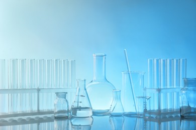 Photo of Laboratory glassware on mirror surface against light blue background