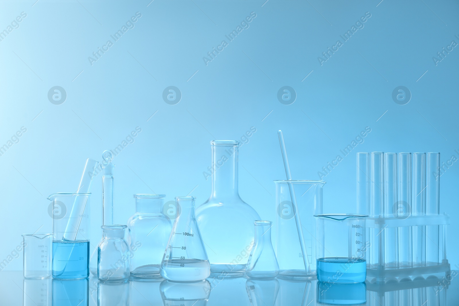 Photo of Laboratory glassware on mirror surface against light blue background