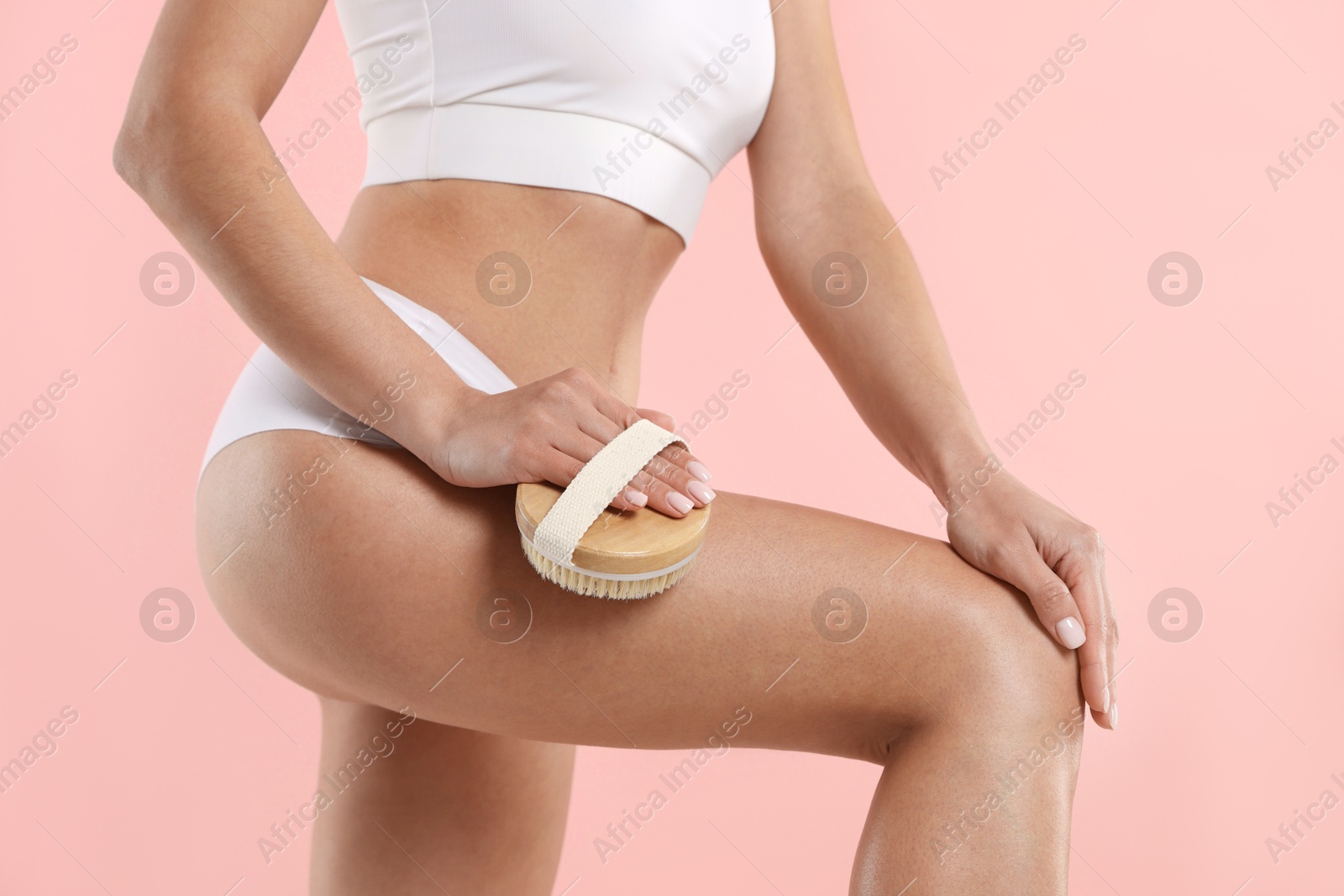 Photo of Woman doing anti cellulite massage with brush on pink background, closeup