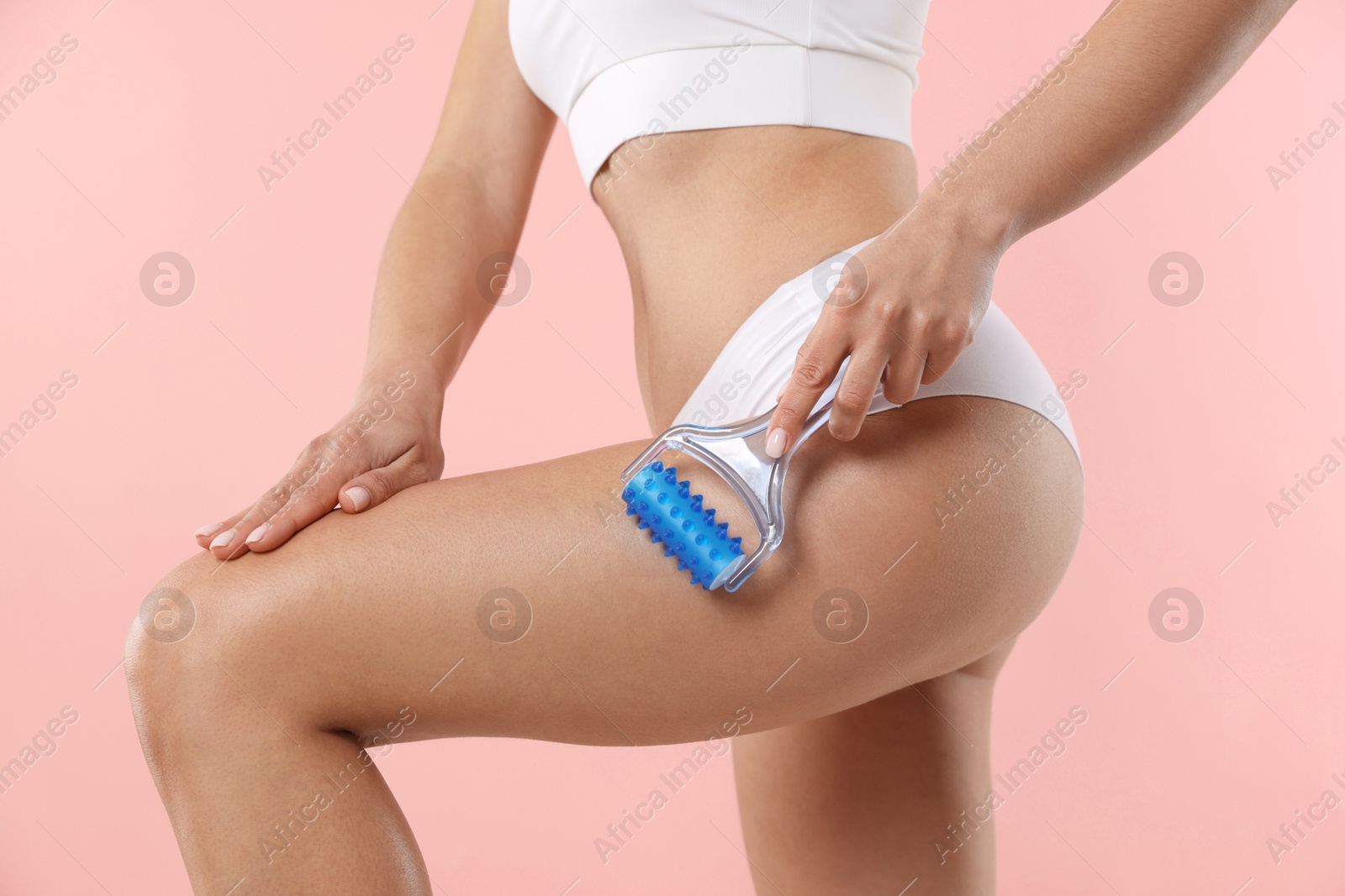 Photo of Woman doing anti cellulite massage with roller on light pink background, closeup