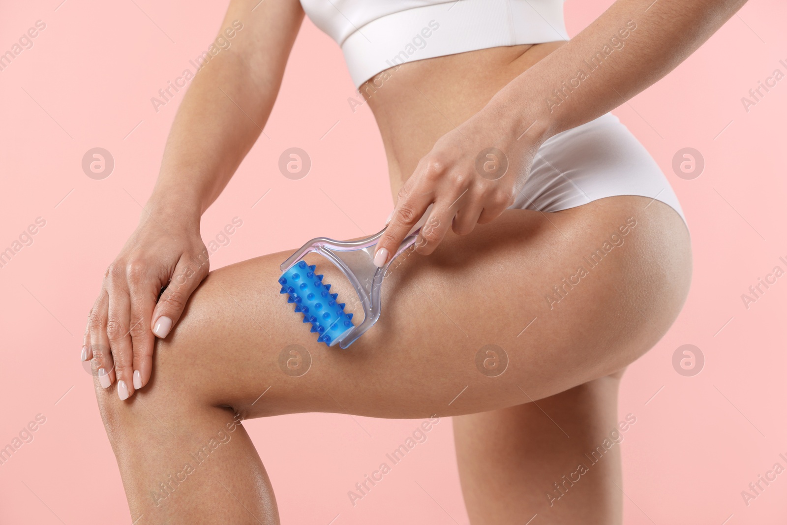 Photo of Woman doing anti cellulite massage with roller on light pink background, closeup