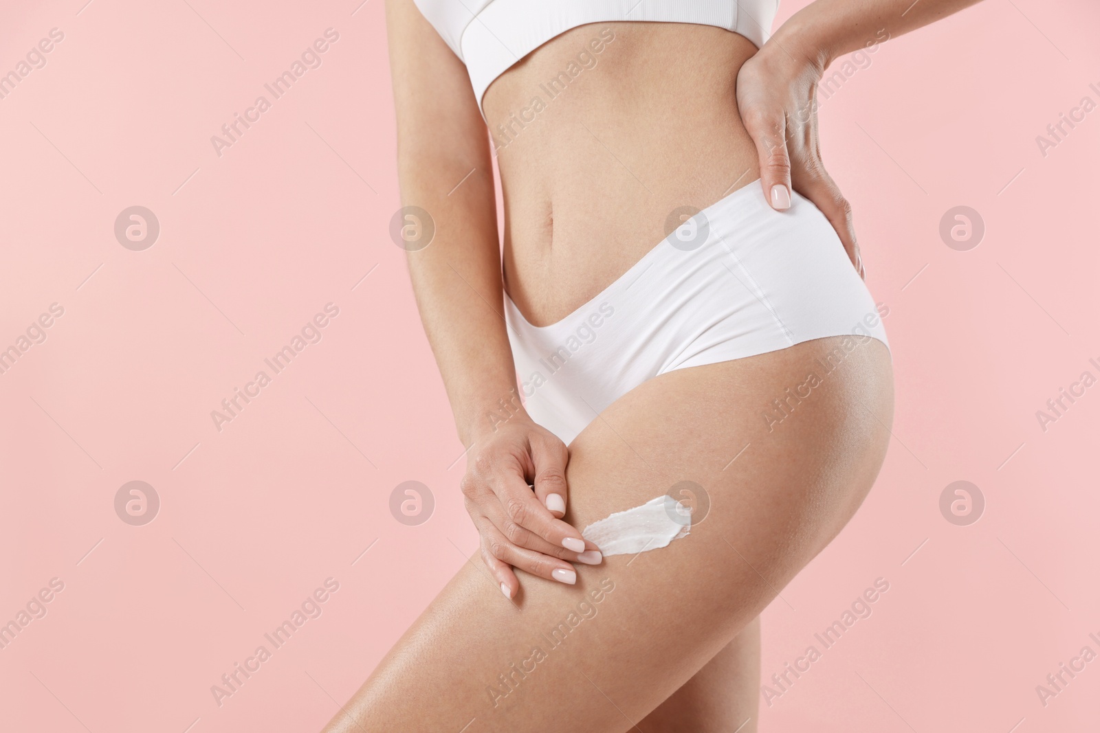 Photo of Woman applying anti cellulite cream on light pink background, closeup. Space for text