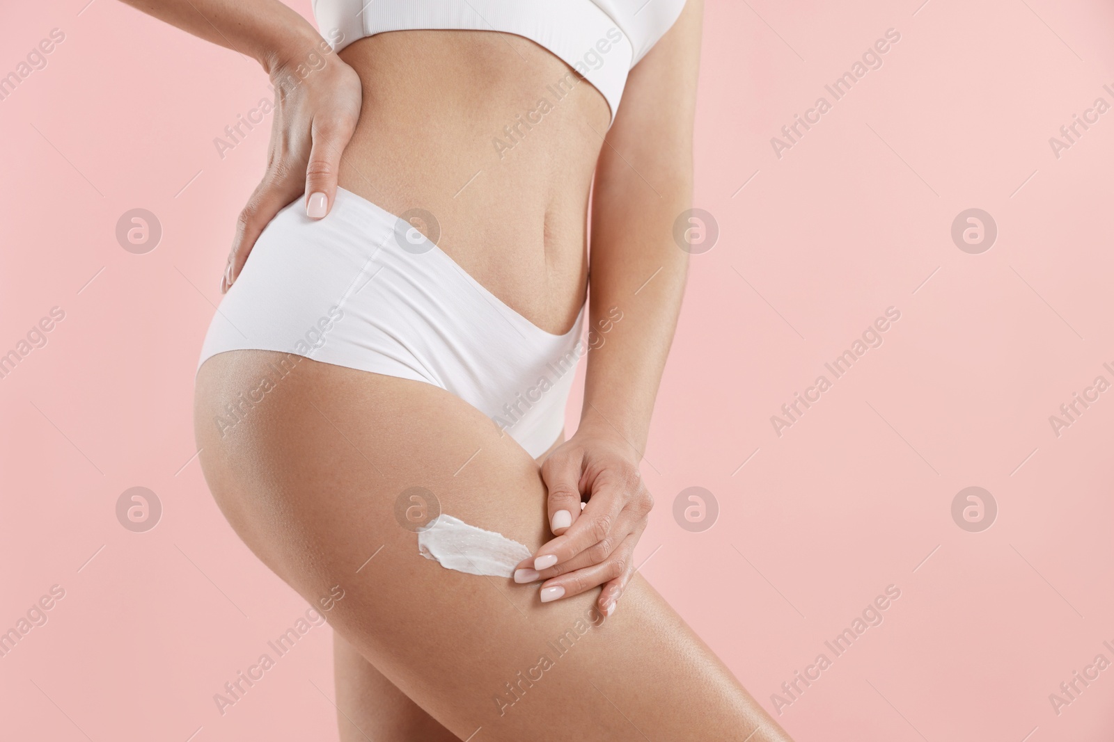 Photo of Woman applying anti cellulite cream on light pink background, closeup. Space for text