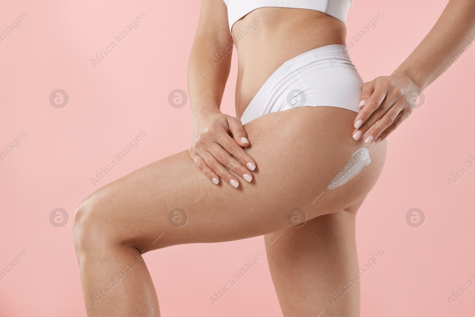 Photo of Woman applying anti cellulite cream on light pink background, closeup