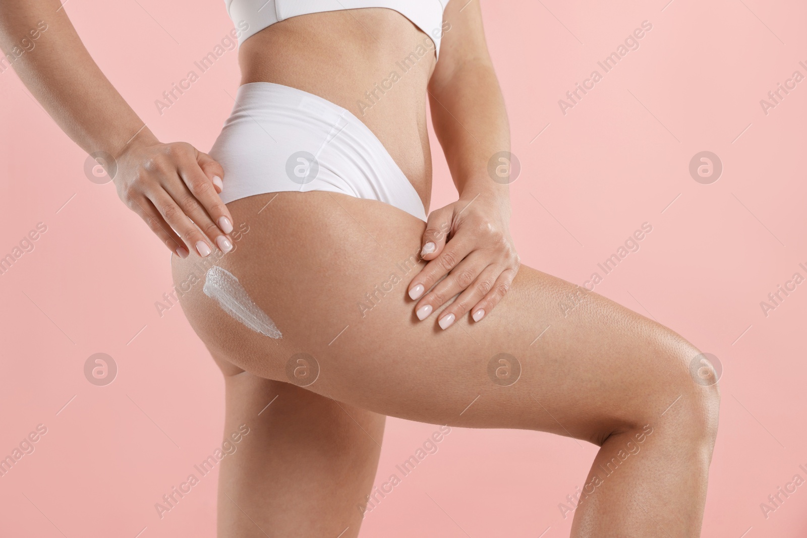 Photo of Woman applying anti cellulite cream on light pink background, closeup