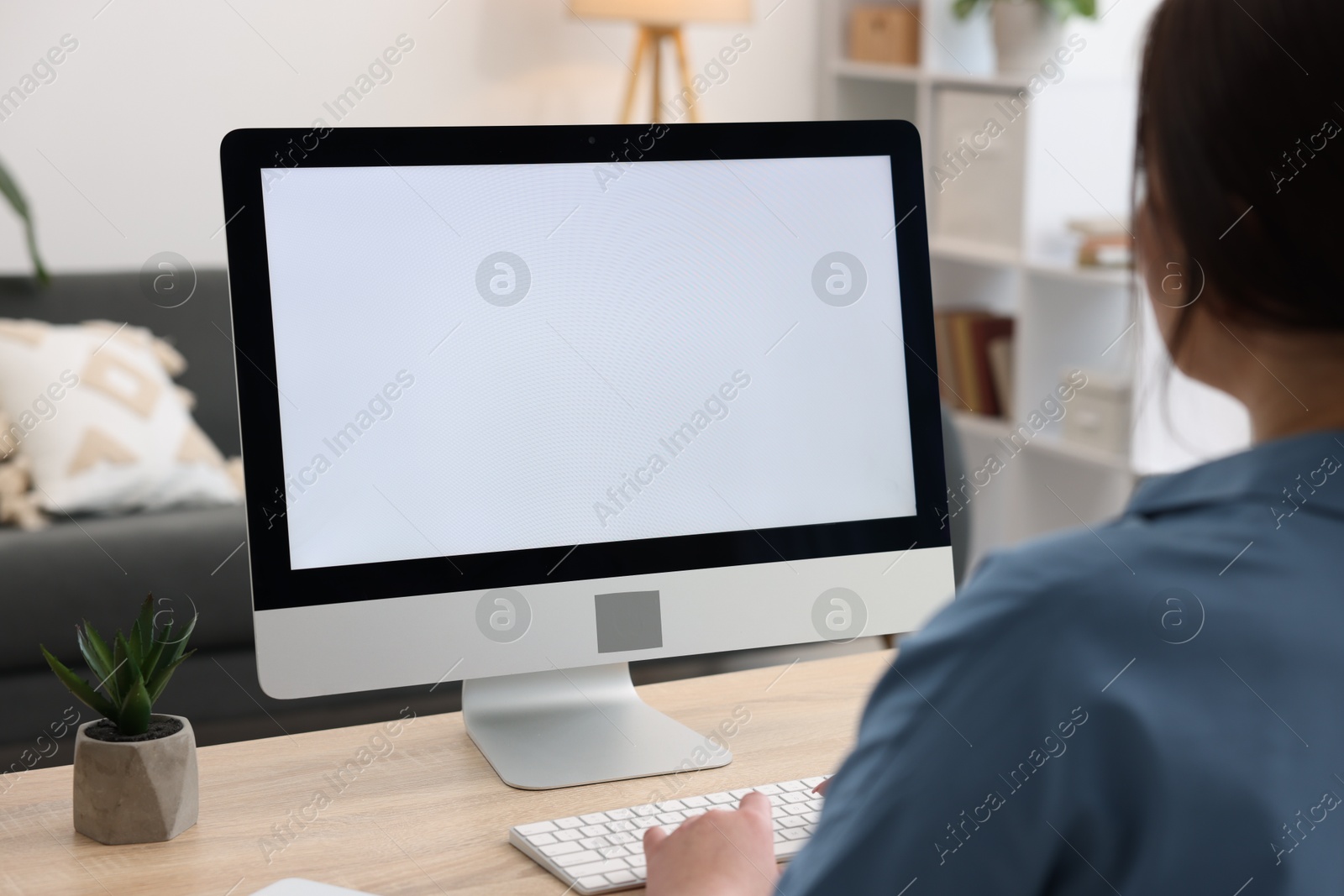 Photo of Woman looking at monitor with blank screen at wooden table indoors. Mockup for design