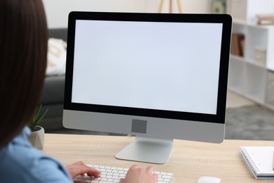 Photo of Woman looking at monitor with blank screen at wooden table indoors. Mockup for design