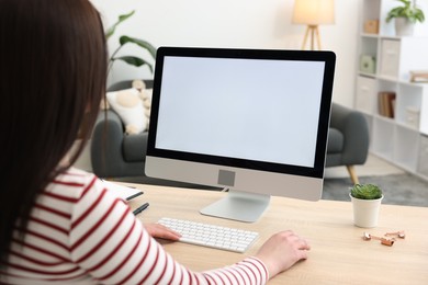 Woman looking at monitor with blank screen at wooden table indoors. Mockup for design