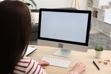 Photo of Woman looking at monitor with blank screen at wooden table indoors. Mockup for design