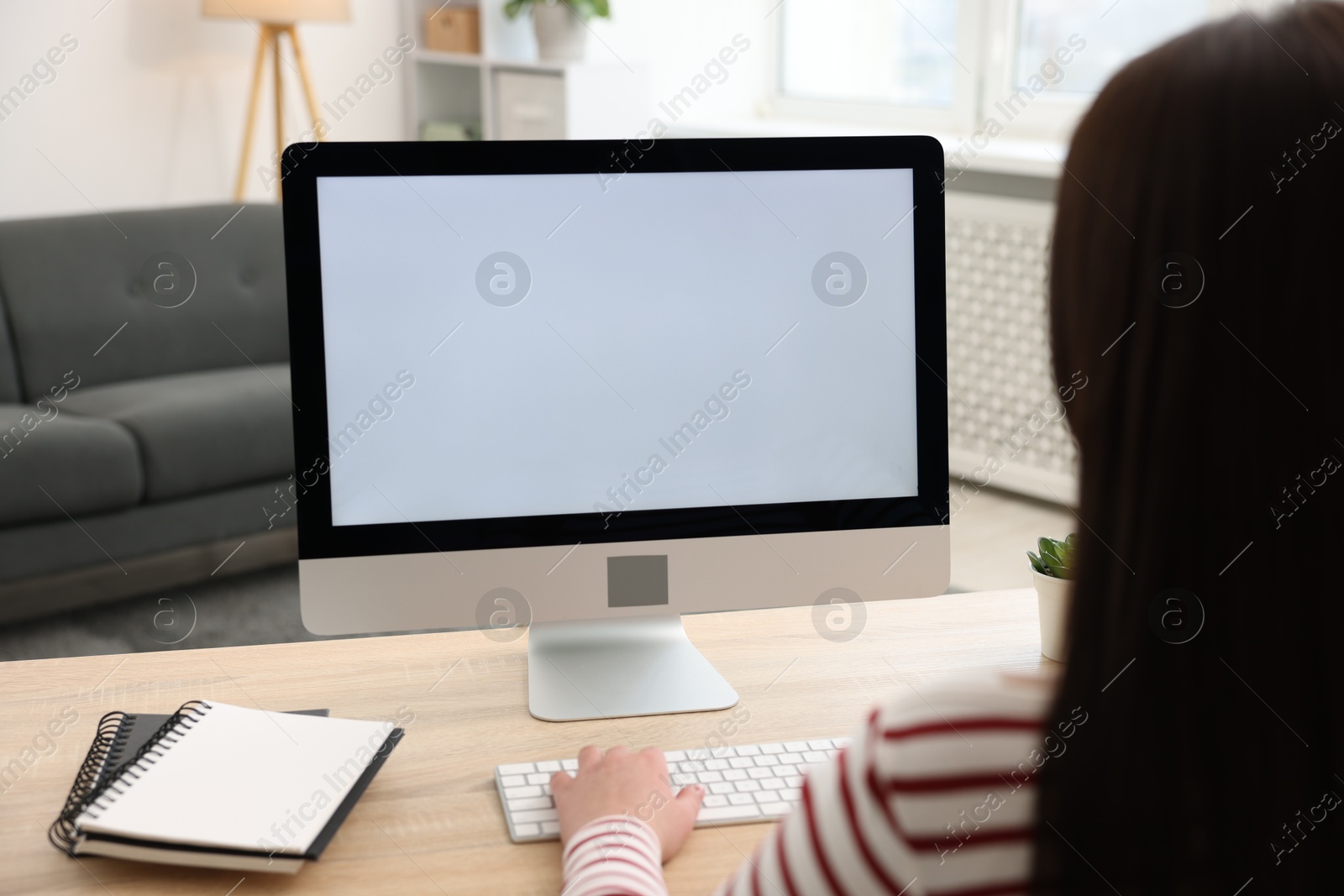 Photo of Woman looking at monitor with blank screen at wooden table indoors. Mockup for design