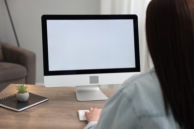 Woman looking at monitor with blank screen at wooden table indoors. Mockup for design