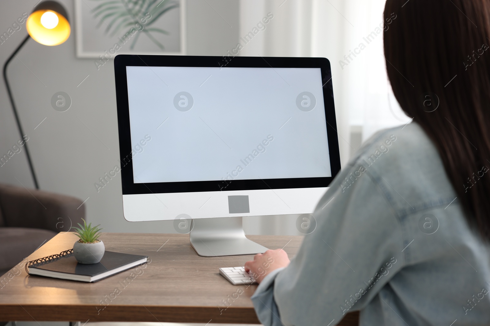 Photo of Woman looking at monitor with blank screen at wooden table indoors. Mockup for design