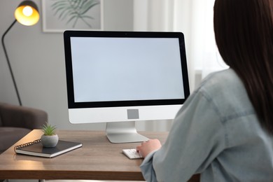 Photo of Woman looking at monitor with blank screen at wooden table indoors. Mockup for design