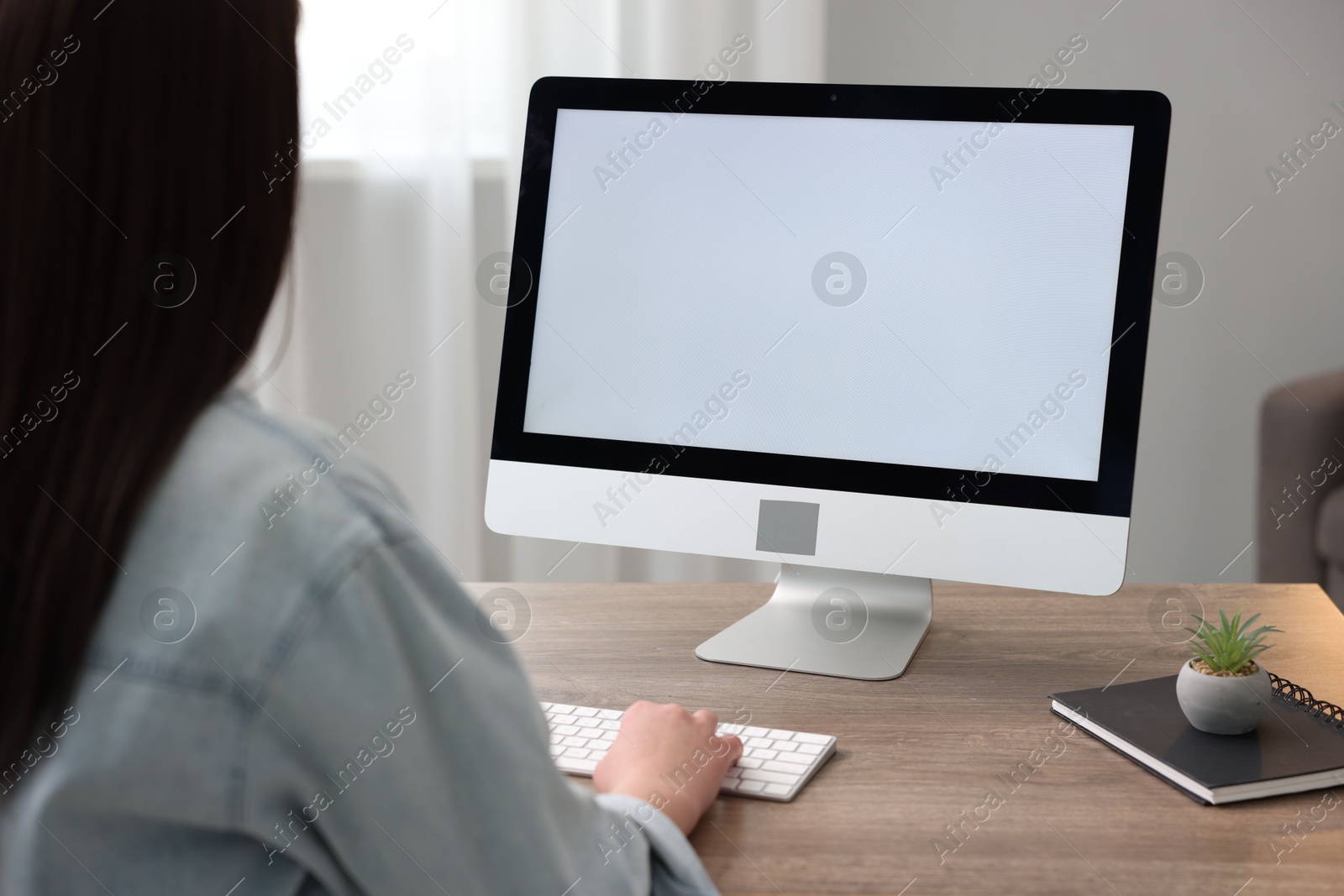 Photo of Woman looking at monitor with blank screen at wooden table indoors. Mockup for design