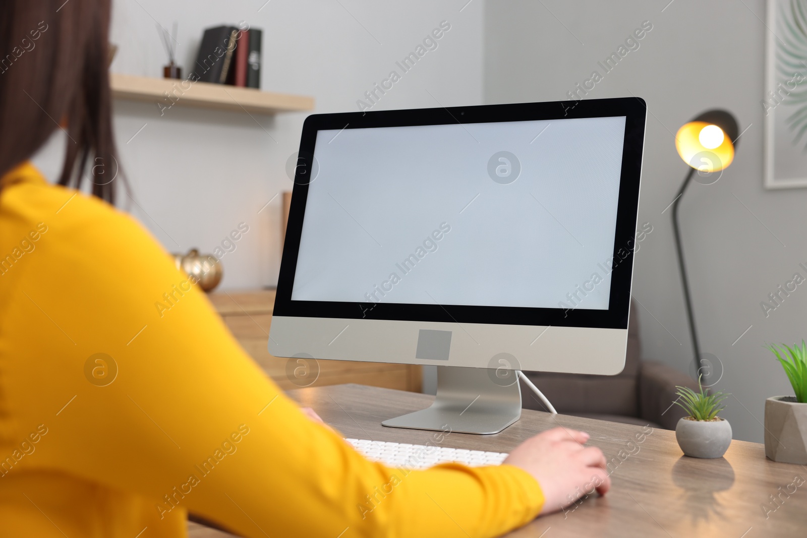 Photo of Woman looking at monitor with blank screen at wooden table indoors, closeup. Mockup for design