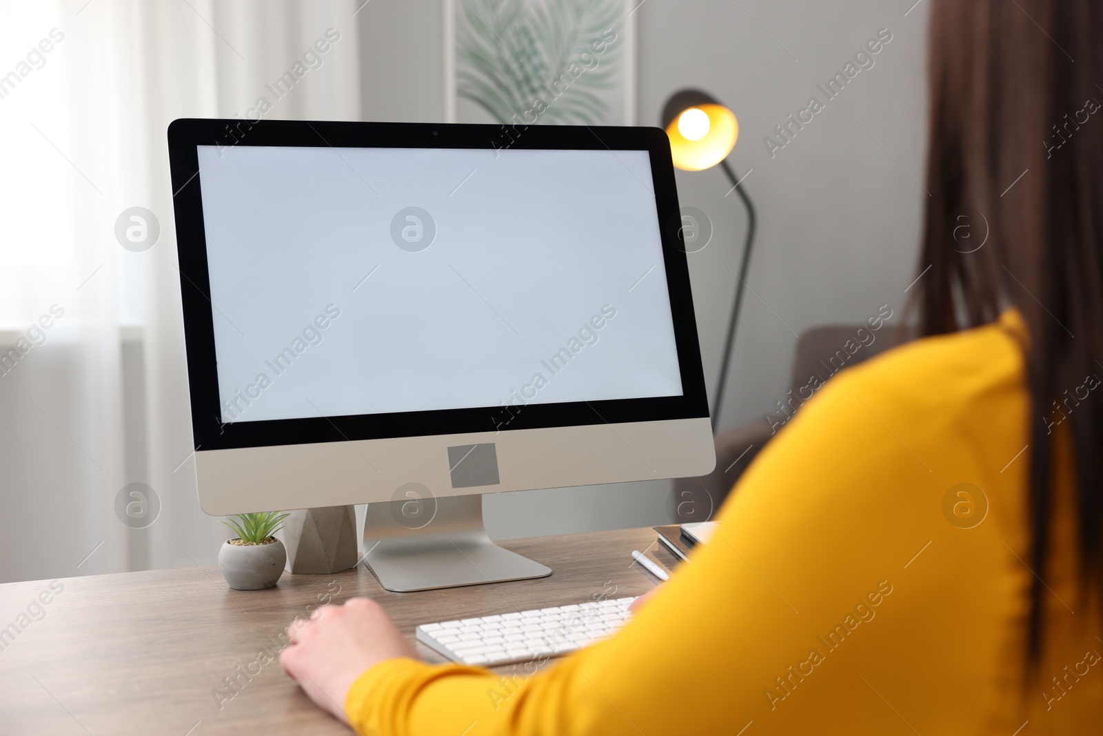 Photo of Woman looking at monitor with blank screen at wooden table indoors, closeup. Mockup for design