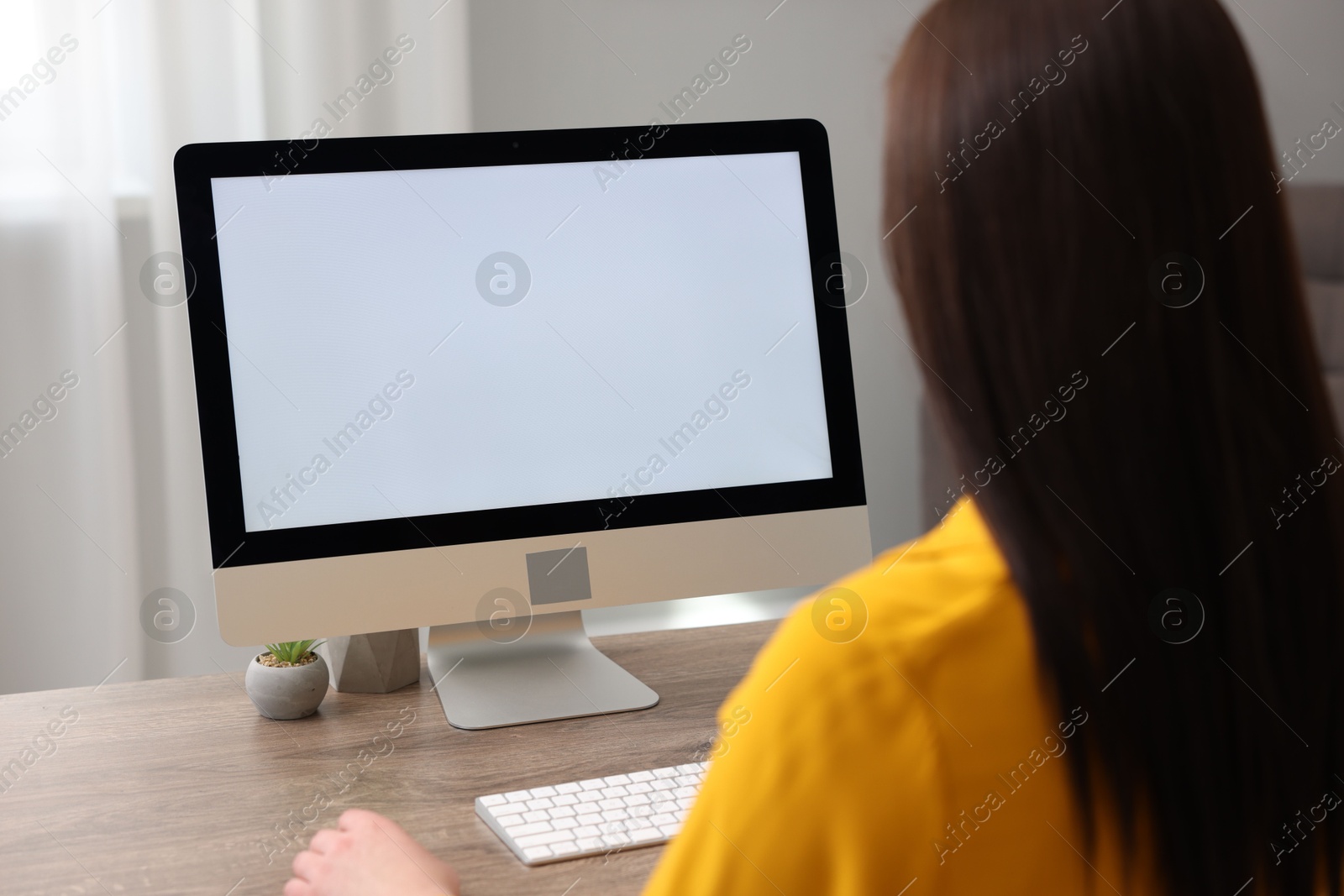 Photo of Woman looking at monitor with blank screen at wooden table indoors. Mockup for design