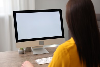 Photo of Woman looking at monitor with blank screen at wooden table indoors. Mockup for design