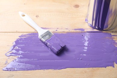 Photo of Smear of violet paint, can and brush on wooden table, closeup